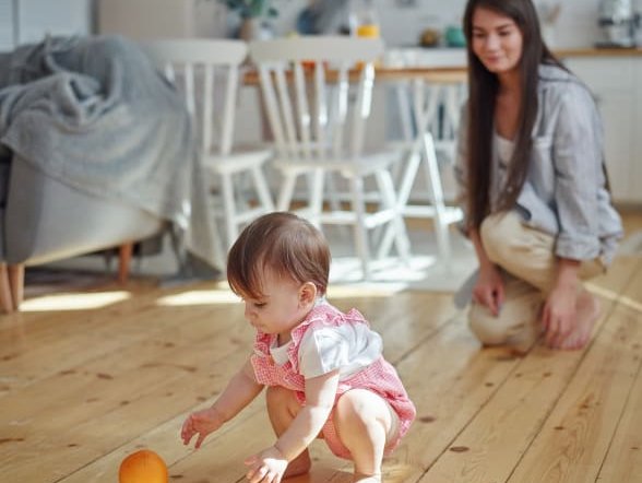 A mother and her baby playing on a hardwood floor